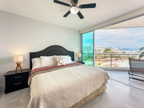 Un dormitorio con una cama grande, ventilador de techo y vista a una piscina y edificios.