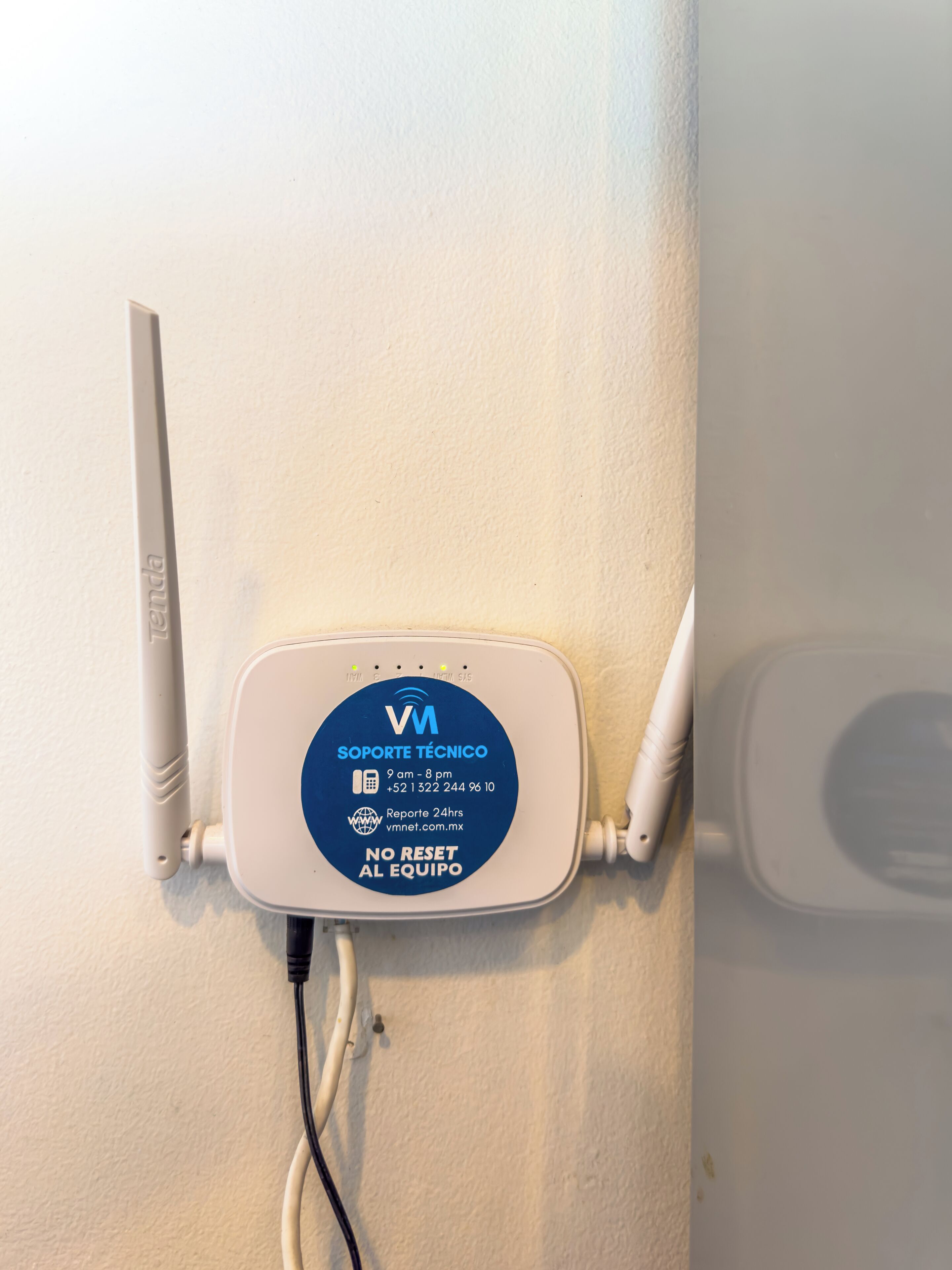 A white wall-mounted device with two antennas, a power cord, and a label with technical support contact information.