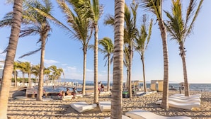 Una playa con palmeras, sillas de descanso y una zona de piscina.