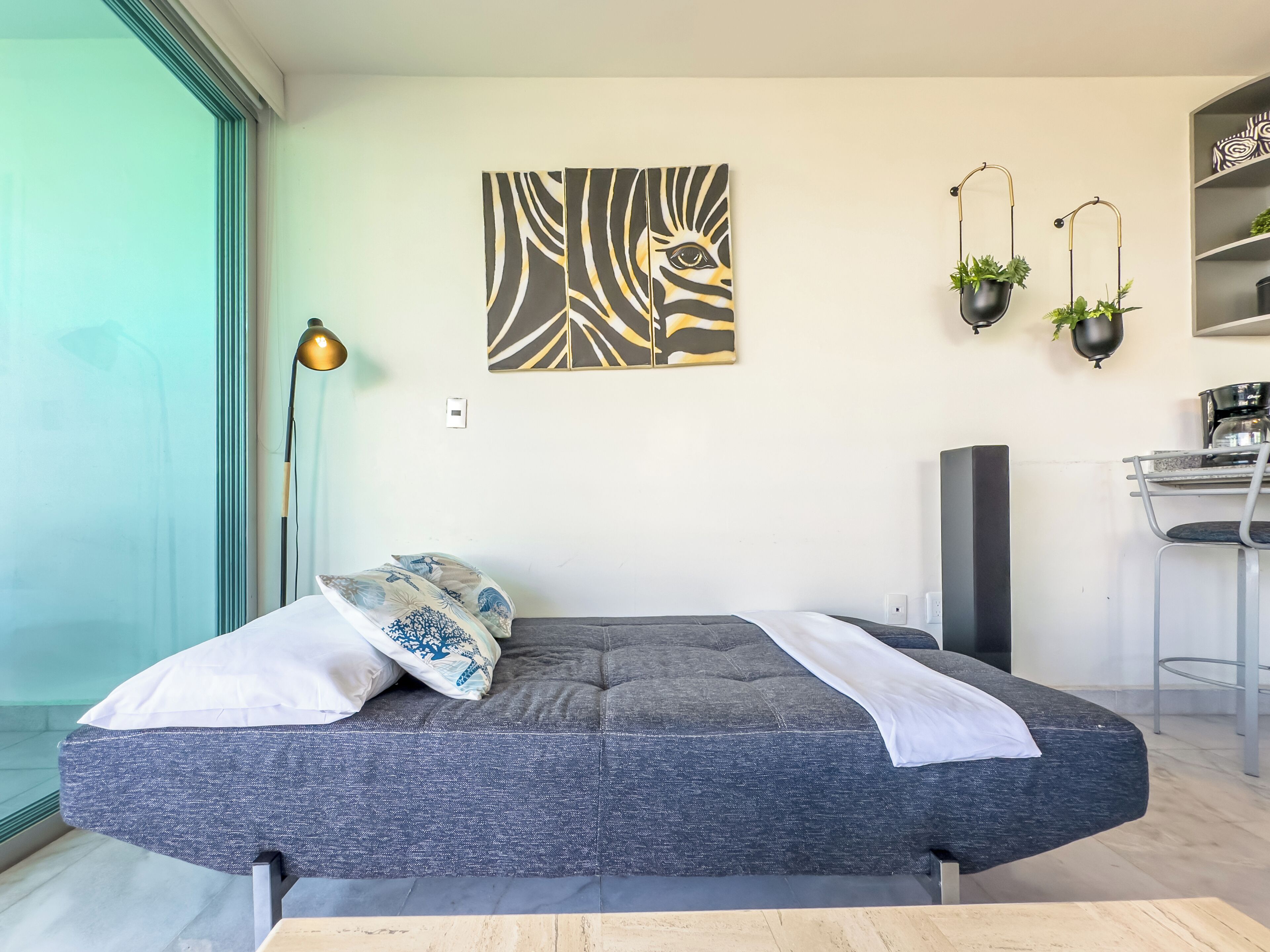 Una camera da letto moderna con un divano letto grigio, un grande quadro astratto, una scrivania con una sedia e due vasi pensili.