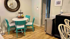 Cocina compacta con una mesa redonda, sillas color turquesa, un refrigerador y un espejo en la pared.