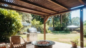 Eine Außenpatio-Terrasse mit einem Steinkamin, Korbstühlen und einem Grill.