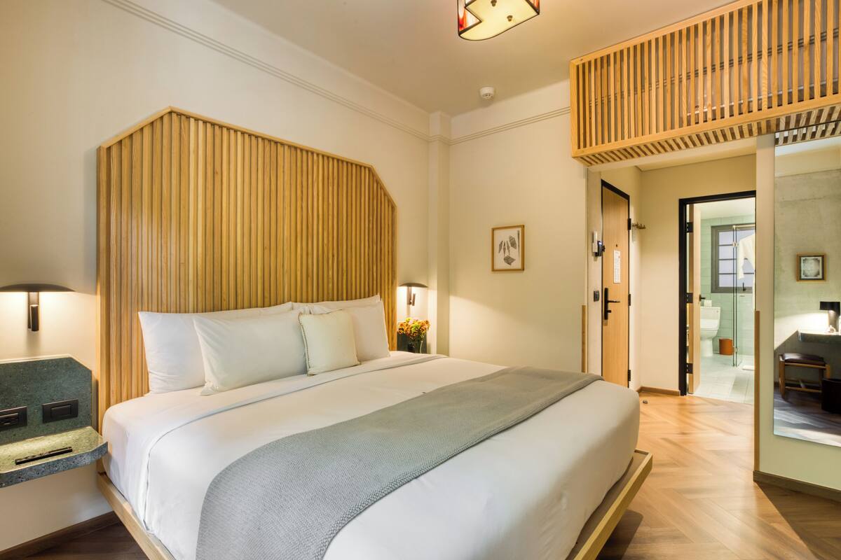 A modern hotel room with a large bed, wooden headboard, bedside tables, and a view of the bathroom.