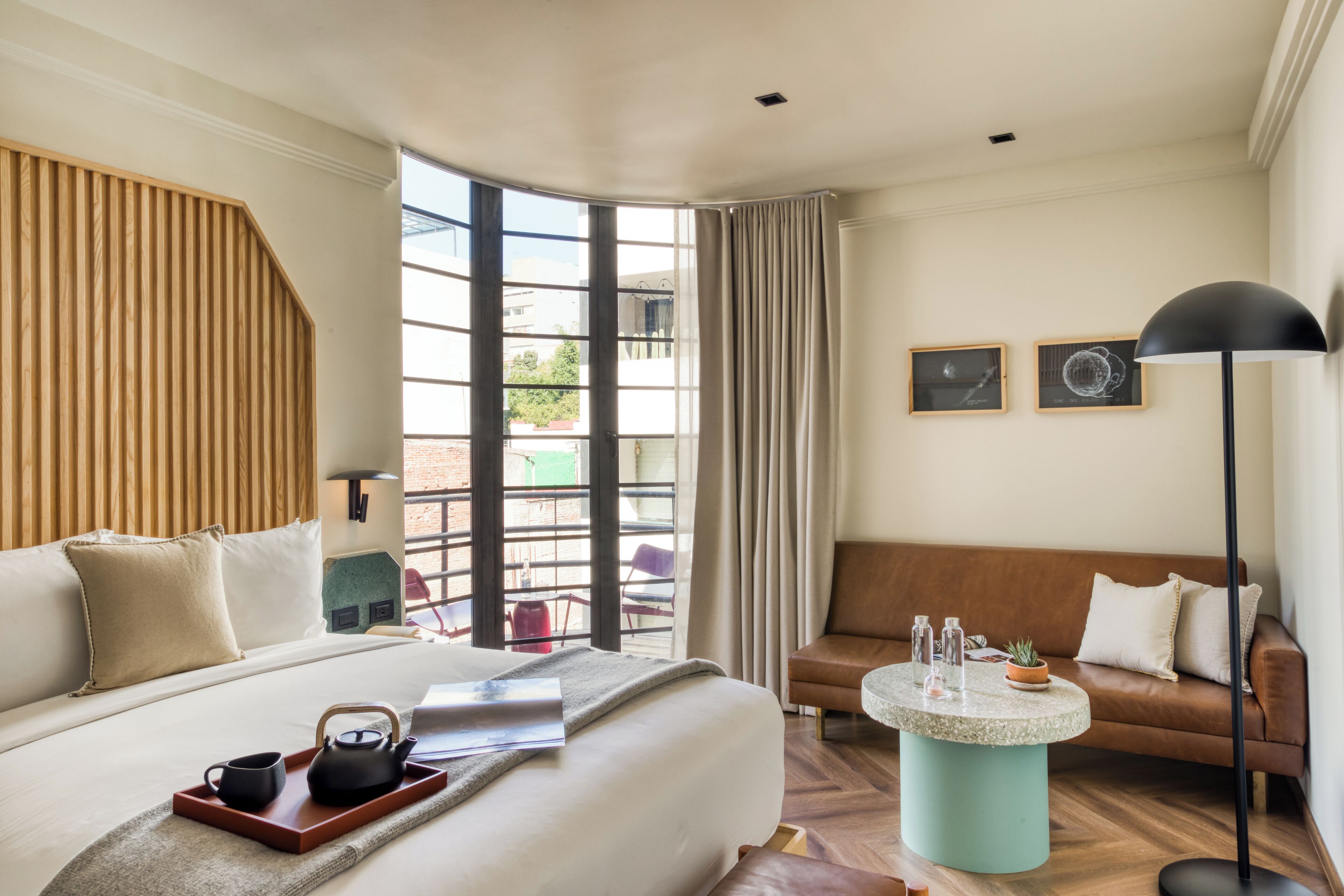 A hotel room with a large bed, a sofa, a small round table with a lamp, and a view of the outdoors.