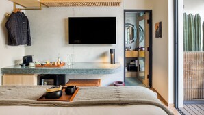 Une chambre d’hôtel moderne équipée d’un lit, d’un téléviseur fixé au mur, d’un plafond en bois, d’un coin cuisine avec un comptoir et d’une porte-fenêtre coulissante donnant sur un balcon.