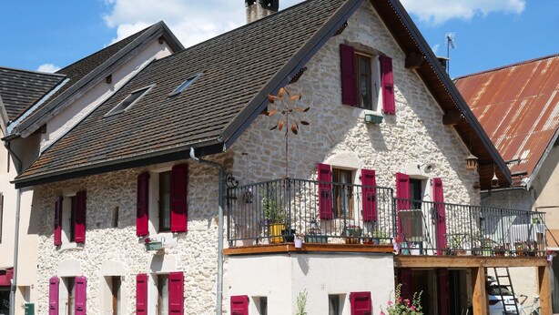 Ein Gebäude aus Stein mit roten Fensterläden, einem Balkon und einem Metallgeländer.