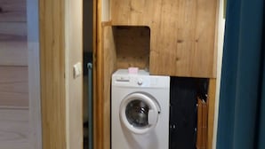 Ein kleiner Waschraum mit einer Waschmaschine, Holzausbau und Fliesenboden.