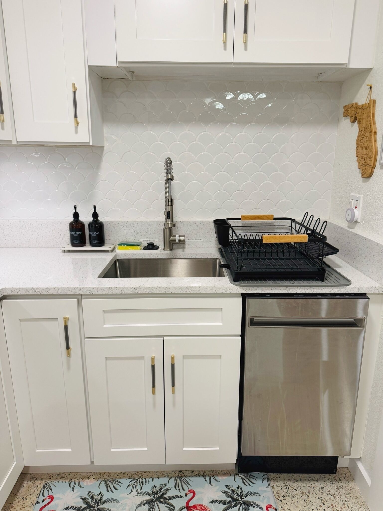 A kitchen with white cabinets, a stainless steel sink, and a dishwasher. There are two soap dispensers on the counter.