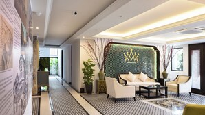 A modern hotel lobby with a patterned floor, a seating area with a sofa and armchairs, a decorative wall with a crown motif, and a potted plant. - The Leith (George Town)