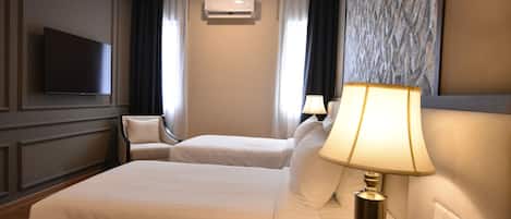 Habitación de hotel con dos camas, un televisor montado en la pared, un aire acondicionado y una lámpara en la mesita de noche.