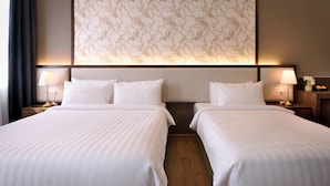 Habitació d'hotel amb dos llits, cadascun amb roba de llit blanca i un edredó rayat. Hi ha taules de nit amb làmpades i un ram de flors. Un mural amb un dibuix floral gran presideix la paret sobre els llits.