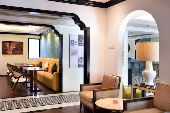 A hotel lobby with a sofa, chairs, a table, and an information board. - The Leith (George Town)