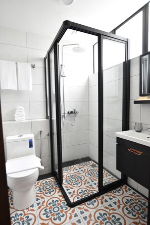 A modern bathroom with a glass-enclosed shower, a white toilet, and a sink with a black cabinet. - The Leith (George Town)