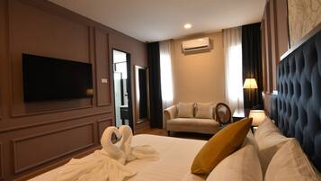 Quarto de hotel com cama, televisão de tela plana, sofá, poltrona e abajur.