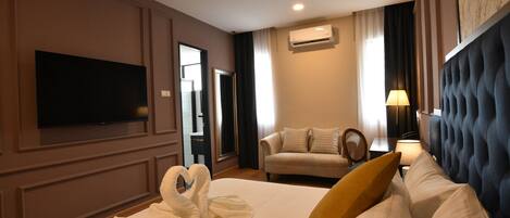 Habitación de hotel con cama, televisor de pantalla plana, sofá, sillón y lámpara.
