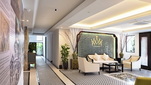 Un rebedor d'hotel modern amb un sòl estampat, una zona de seients amb un sofà i butaques, una paret decorativa amb un motiu de corona i una planta en test.