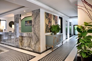 A hotel reception area with a marble reception desk, a clock, and a large plant. - The Leith (George Town)
