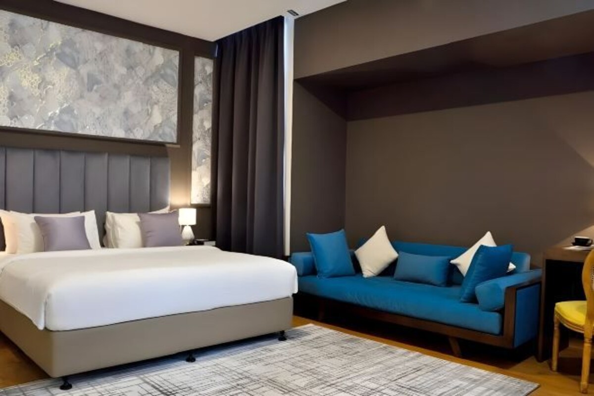 Ett modernt hotellrum med en stor säng, en blå soffa och en vägg av marmor.