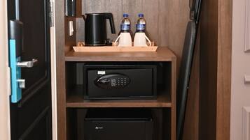 Uma cozinha compacta equipada com cafeteira, duas garrafas de água, chaleira, micro-ondas e pequena geladeira.
