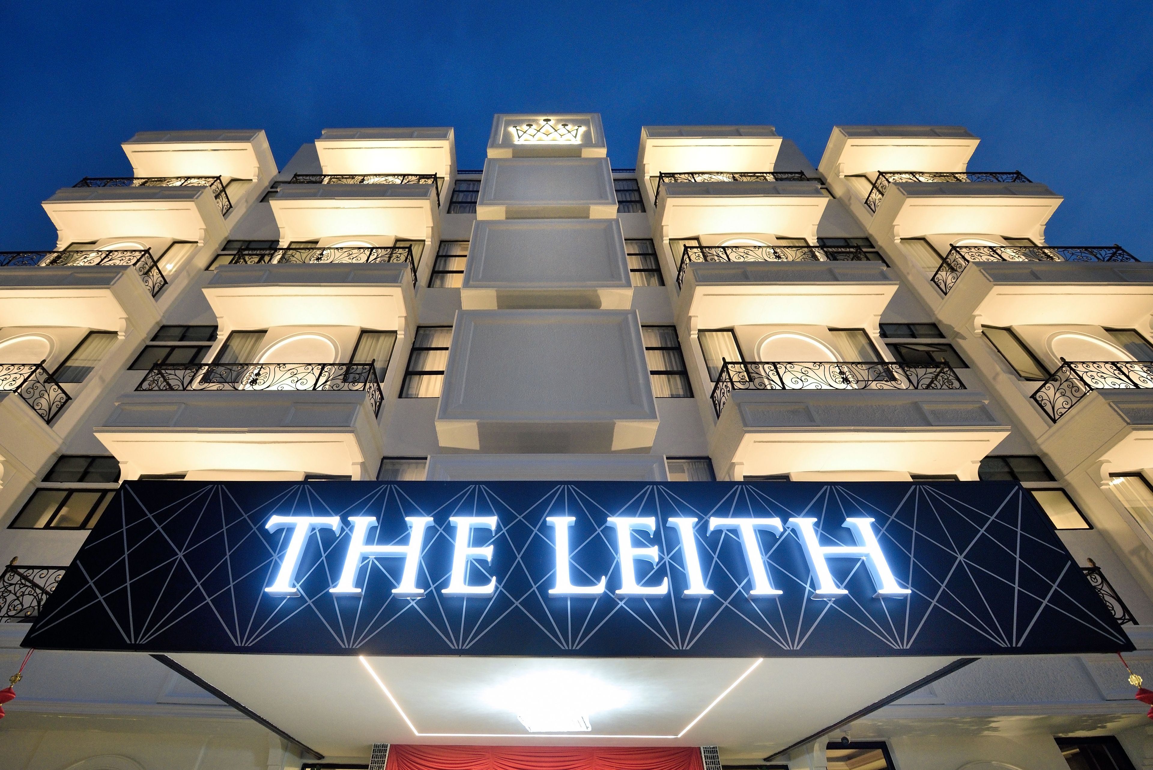 Um hotel com uma placa iluminada de destaque com a inscrição 'THE LEITH' e um design arquitetônico moderno com sacadas.
