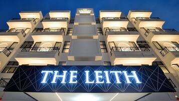 Um hotel com uma placa iluminada de destaque com a inscrição 'THE LEITH' e um design arquitetônico moderno com sacadas.
