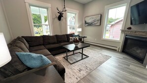 A living room with a sectional sofa, a coffee table, a fireplace, and a mounted deer head. - STAY WITH US, Brand New, 8 BR, 4 Bth, 1/2 mi to Okemo, Hot Tub, on Shuttle, King (Ludlow)