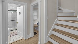 A staircase with wooden steps and white walls, leading to a bathroom with a white toilet and a shower area. - Spacious 5BedRooms House Near Millikin Univ – Perfect for Groups & Families! (Decatur)