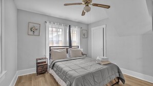 A bedroom with a bed, a ceiling fan, a nightstand, and a window with curtains. - Spacious 5BedRooms House Near Millikin Univ – Perfect for Groups & Families! (Decatur)