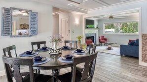 A dining area with a round table, chairs, and a ceiling fan. There is a fireplace and a television in the background. - Casa Contera (St. Augustine)