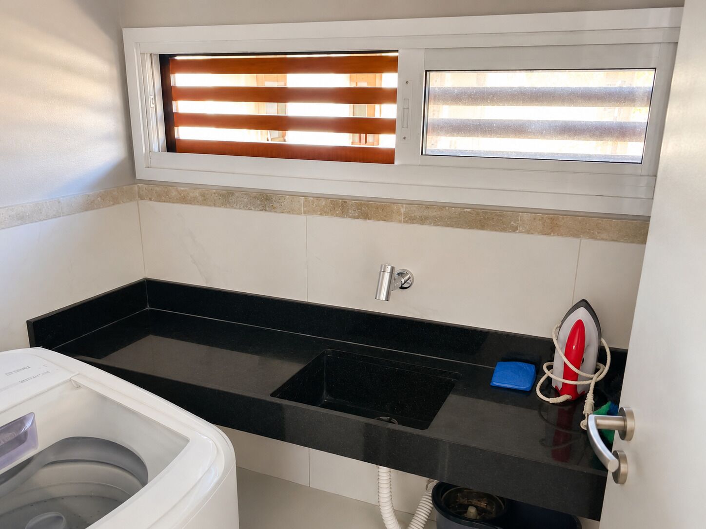 Un bagno con un lavandino nero, un water e una finestra con persiane.