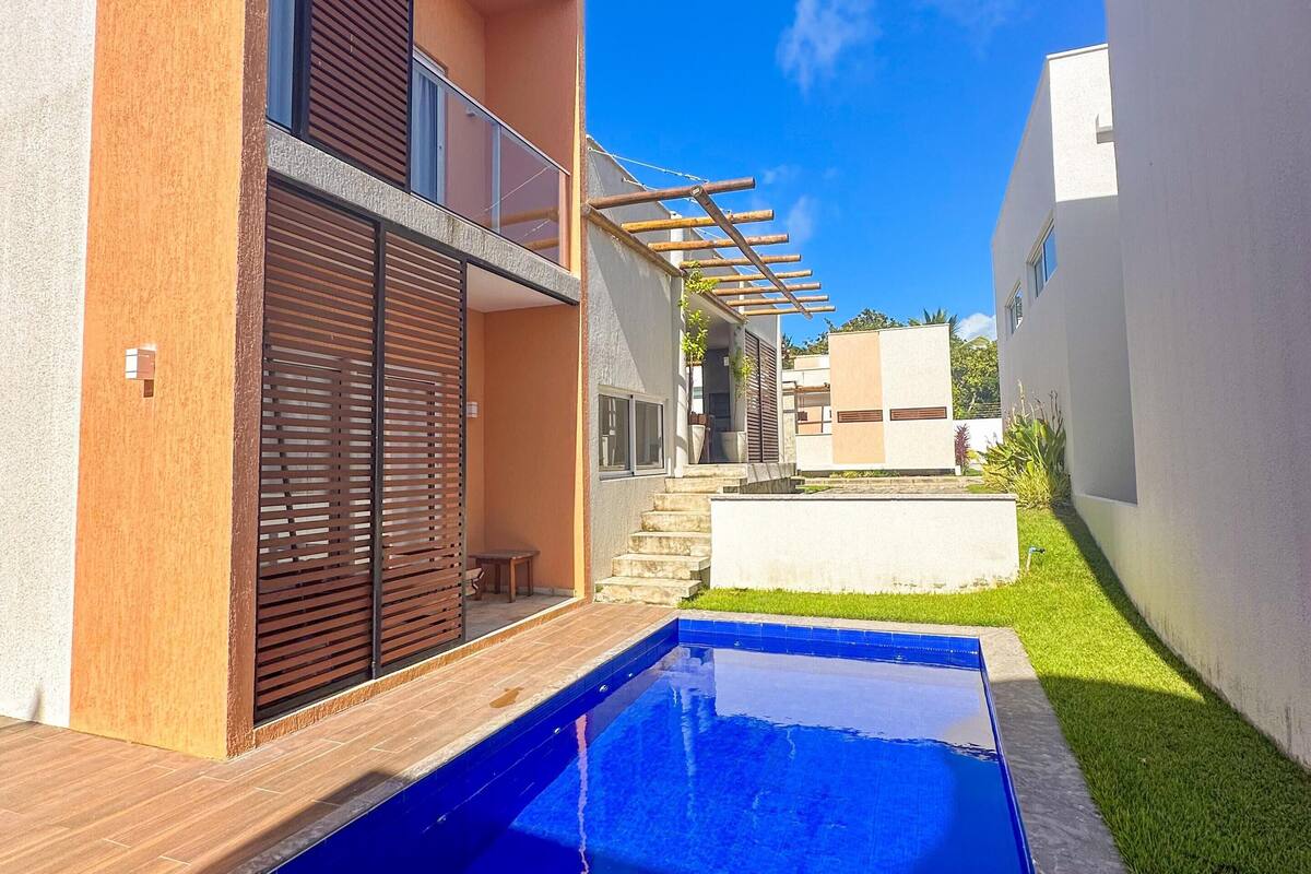 Ein modernes, zweistöckiges Haus mit Swimmingpool, überdachter Terrasse und kleinem Garten.