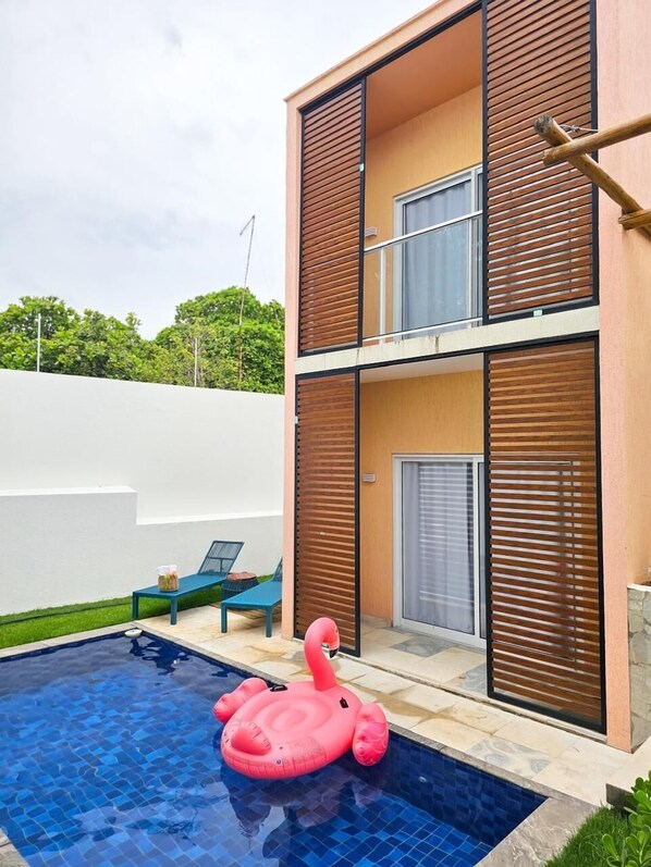 Un edificio moderno de dos pisos con piscina, zona de estar y un flotador de flamenco rosa.