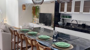 Een moderne keuken met een centraal eiland, barstoelen, een eettafel gedekt met groene borden en wijnglazen, en hanglampen.