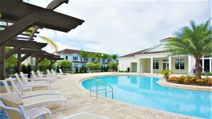A swimming pool with lounge chairs and a covered area, surrounded by buildings and palm trees. - Beautiful Townhouse Next to Disney Parks 24 (Kissimmee)