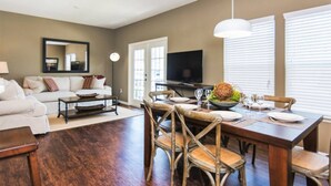 A living room with a dining area, a sofa, a television, and a large window with blinds. - Beautiful Townhouse Next to Disney Parks 24 (Kissimmee)