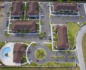 Vue aérienne d’un complexe hôtelier comprenant plusieurs bâtiments, un parking central et une piscine.
