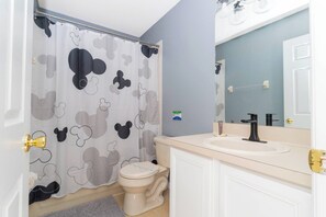 A bathroom with a Mickey Mouse shower curtain, a toilet, a sink, and a mirror.