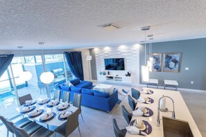 A modern living room with a blue sofa, a TV, and a dining area with a table set for four.