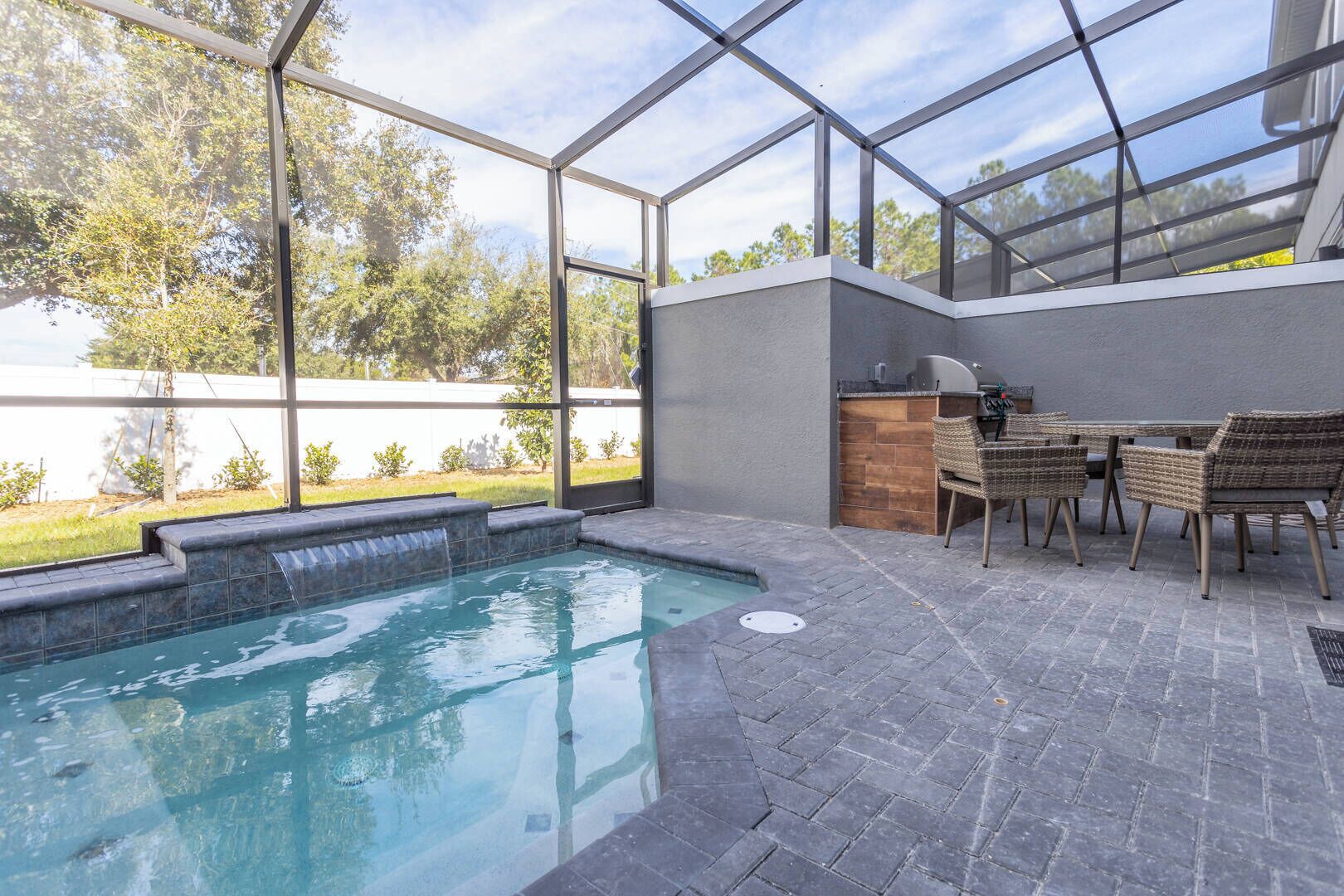 A swimming pool with a glass enclosure, a barbecue area, and outdoor seating.