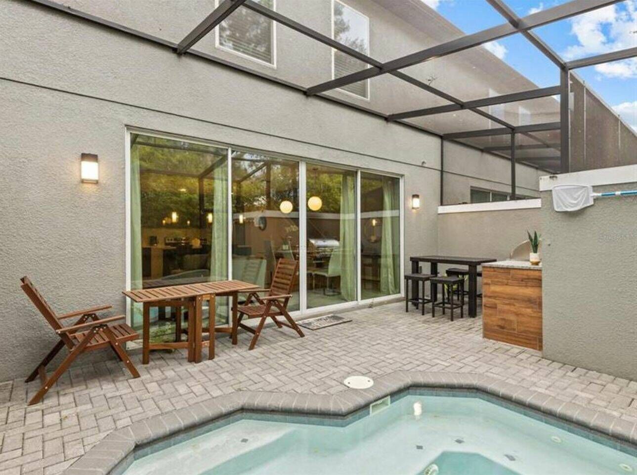 A covered patio with a pool, wooden furniture, and a glass door leading to an interior space.