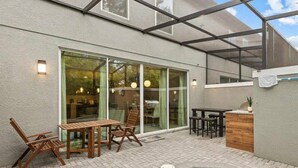A covered patio with a pool, wooden furniture, and a glass door leading to an interior space. - Beautiful Vacation Home With Splash Pool 35 (Kissimmee)