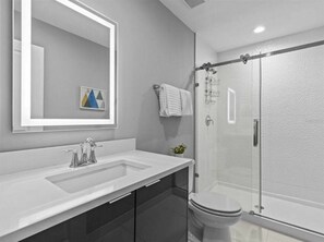 A modern bathroom with a large mirror, a white sink, a glass shower enclosure, and a toilet.