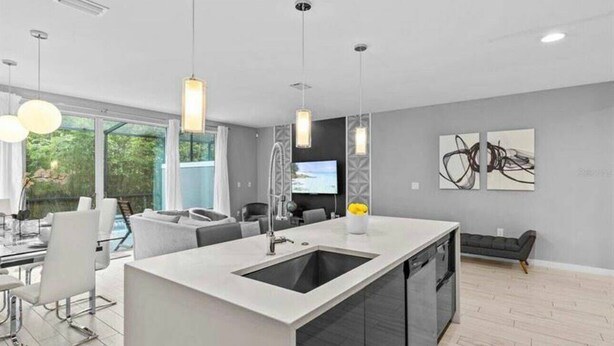 A modern kitchen with a central island, pendant lighting, and a view of the outdoors. - Beautiful Vacation Home With Splash Pool 35 (Kissimmee)