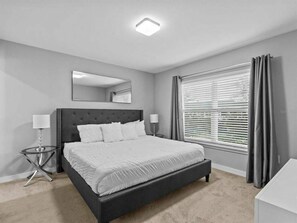 A modern bedroom with a large bed, a bedside table, a nightstand, a mirror, and a window with curtains.