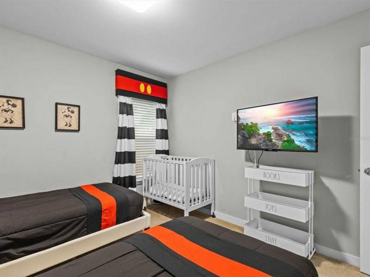 Une chambre avec deux lits, un berceau, une télévision et une bibliothèque.