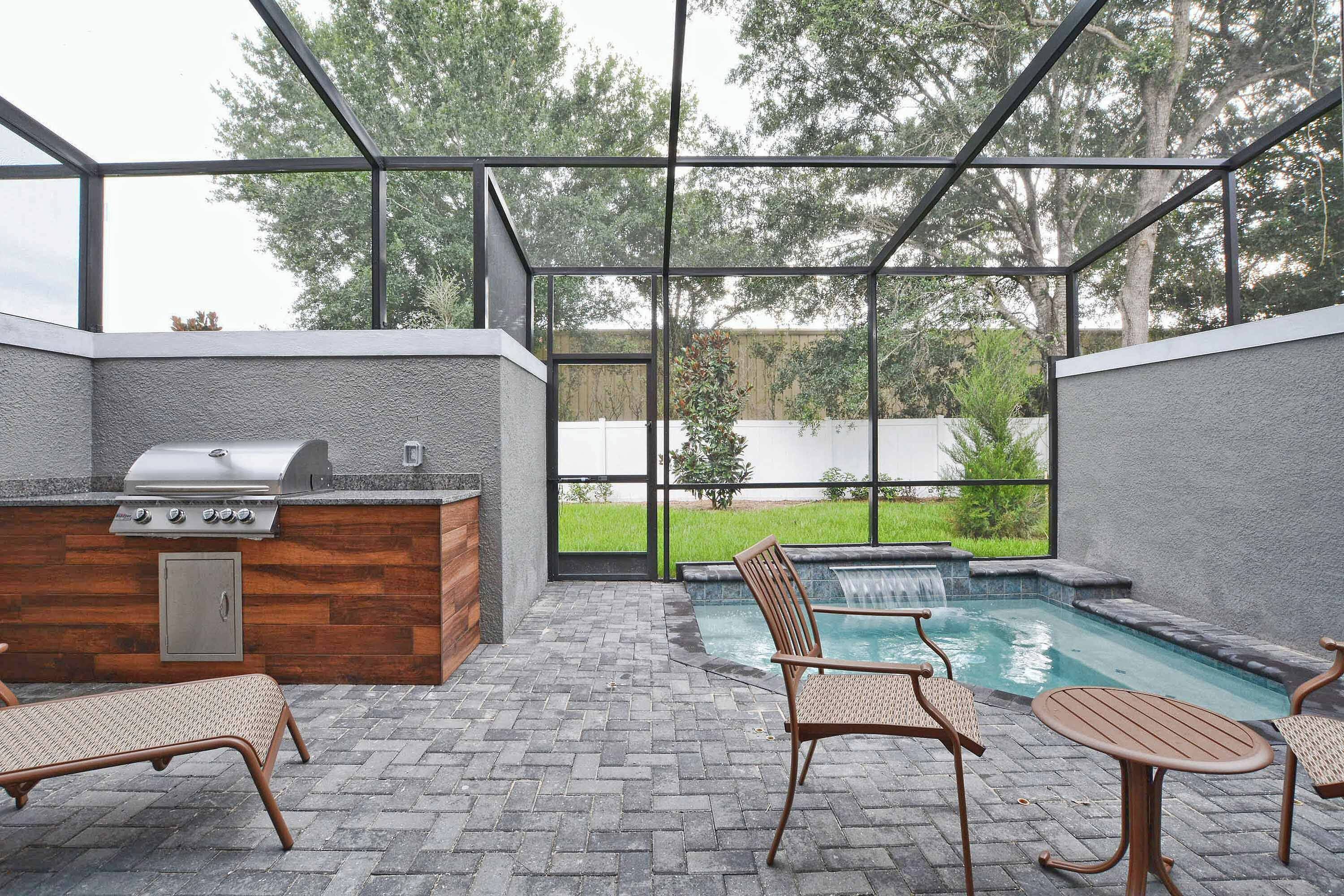 An outdoor patio with a grill, seating, and a small pool.
