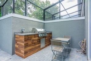 An outdoor kitchen with a grill, a wooden cabinet, and a table with chairs.