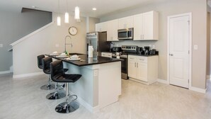 A modern kitchen with white cabinets, stainless steel appliances, and a central island with bar stools. - Free Pool Heat! Last Minute Deal! Near Disney 15 (Kissimmee)