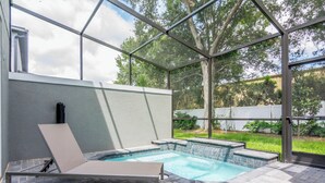 A glass-enclosed outdoor swimming pool with a lounge chair, a hot tub, and a view of the surrounding greenery. - Free Pool Heat! Last Minute Deal! Near Disney 15 (Kissimmee)