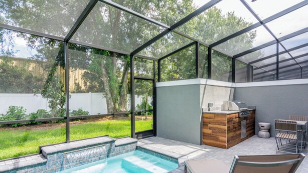 A covered outdoor swimming pool with a wooden deck and a barbecue area. - Free Pool Heat! Last Minute Deal! Near Disney 15 (Kissimmee)